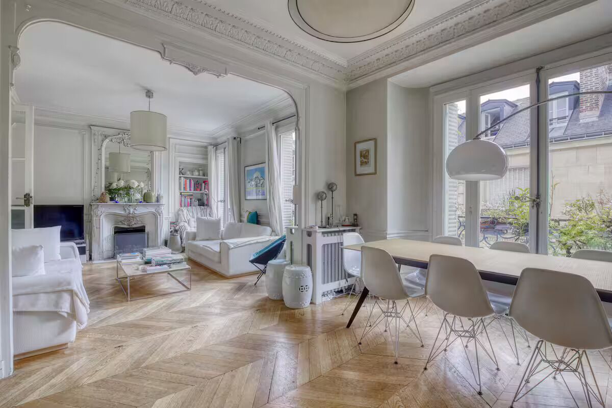 A spacious living area with a fireplace, white furniture, and large windows.