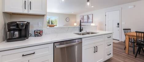 A modern kitchen with white cabinets, a dishwasher, a coffee maker, and pendant lighting.