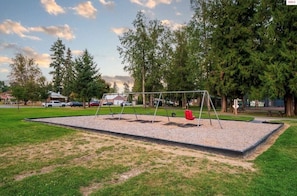 A playground with swings and a red ball, surrounded by trees and a parking lot. - South Sandpoint Condo Near Lake + Downtown (Sandpoint)