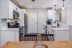 Une cuisine moderne avec des meubles blancs, des appareils en acier inoxydable, une table à manger en bois et des chaises noires.
