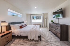 Une chambre à coucher comprenant un lit, une table de chevet, une lampe, une commode, un téléviseur, une fenêtre et une vue sur les arbres.