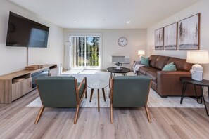 Un salon moderne comprenant un canapé, deux fauteuils, une table basse et un téléviseur fixé au mur.