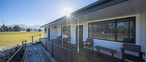 A building with a covered outdoor area, benches, and a view of a field and mountains.