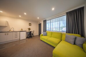 A modern living room with a yellow sofa, a kitchen area with cabinets, and a dining table. - Dusky Fishing Unit - Te Anau Holiday Home (Te Anau)