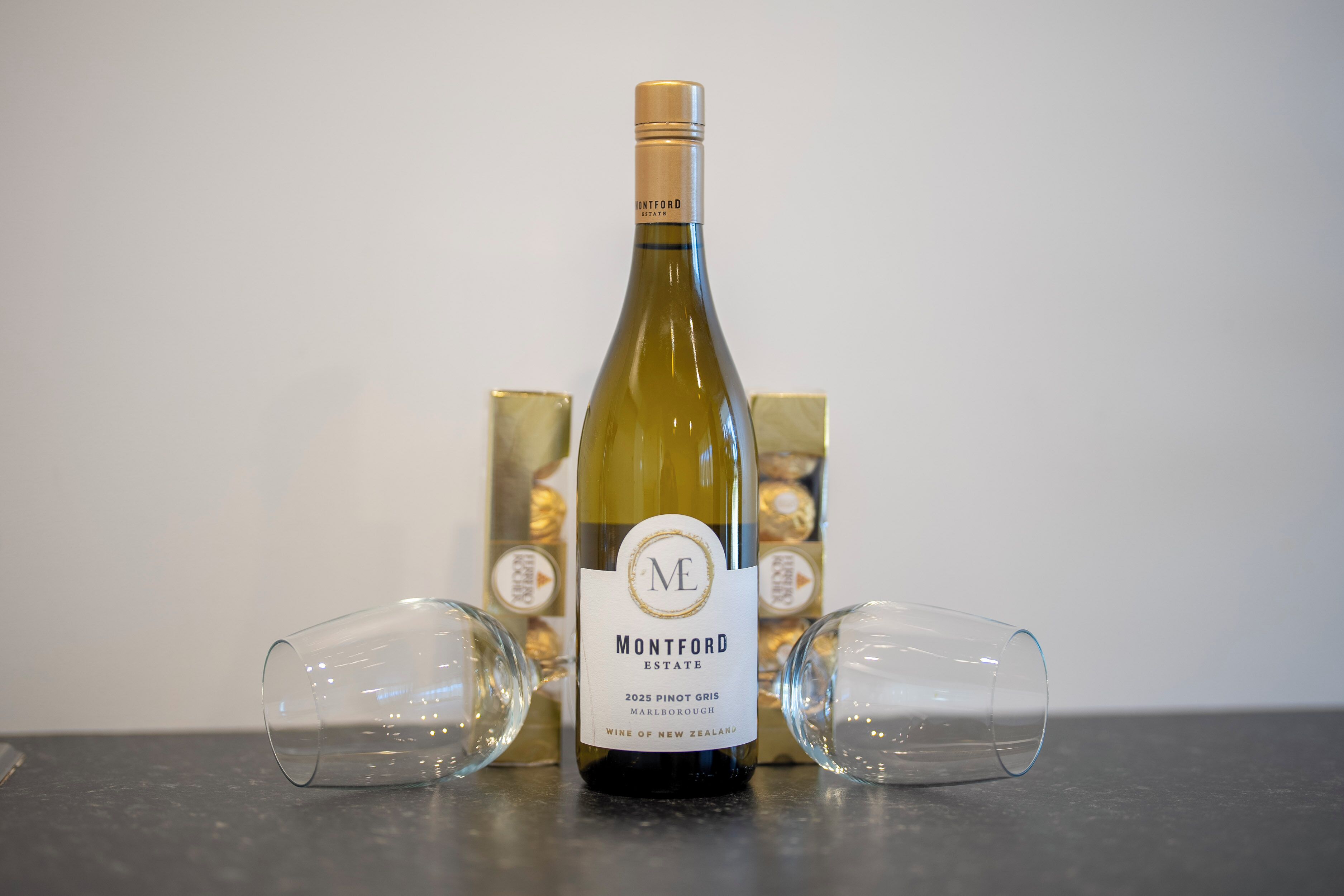 Une bouteille de vin avec une étiquette, deux verres à vin vides et une boîte de chocolats.