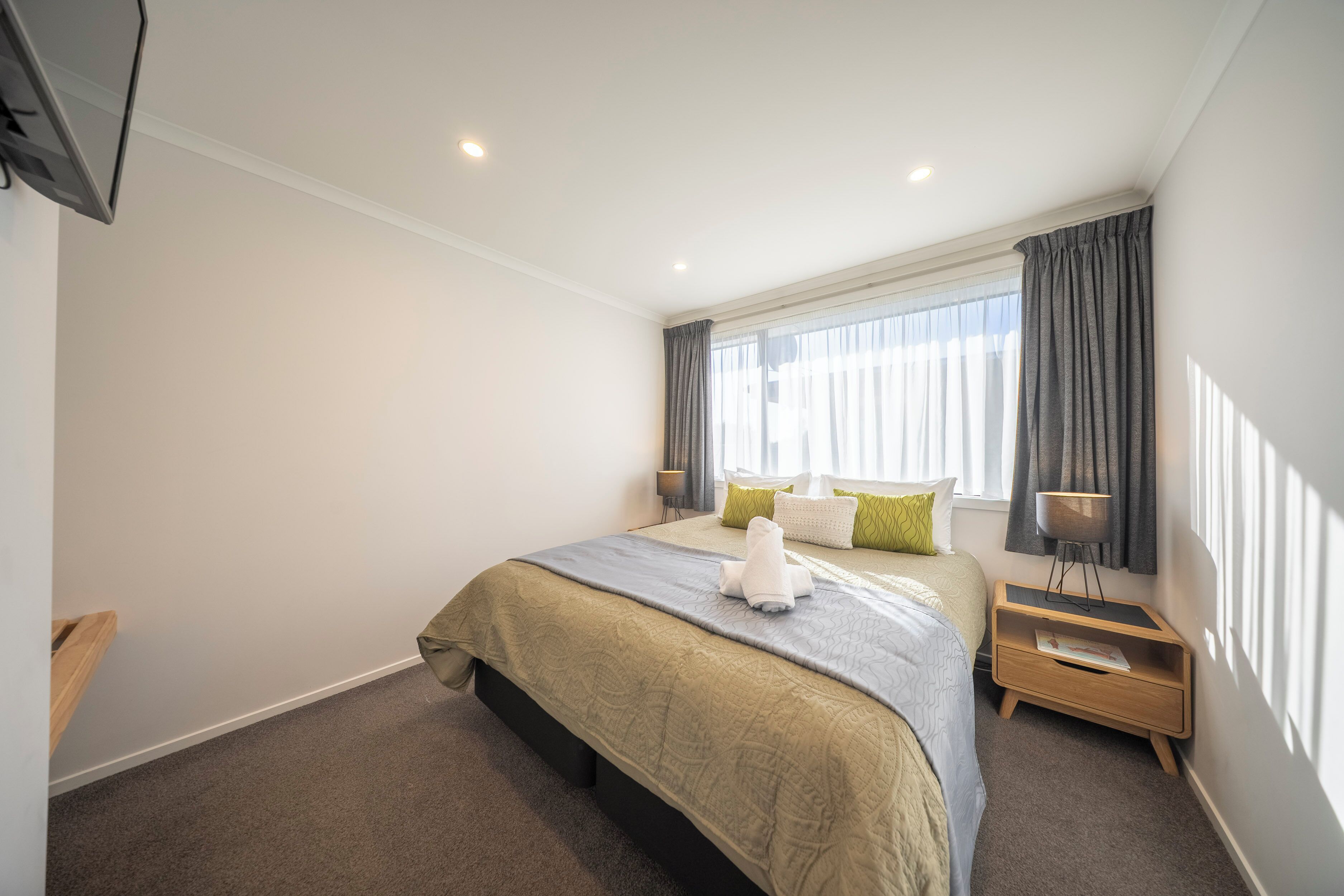 A modern bedroom with a large bed, a bedside table, a lamp, and a window with curtains.