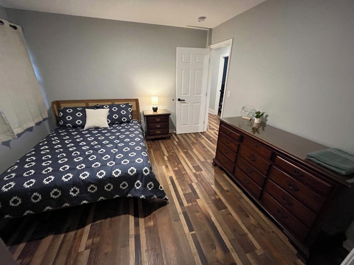 Une chambre à coucher avec un lit, une commode, une table de chevet et une porte.
