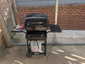 Un barbecue d’extérieur noir, doté d’un panneau de commande, d’une bouteille de propane et d’un support pour menu, le tout mont é sur un socle en métal.