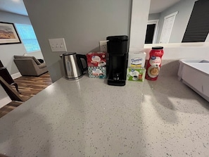 A kitchen counter with a coffee maker, a kettle, a box of cereal, a carton of milk, and a bottle of juice.