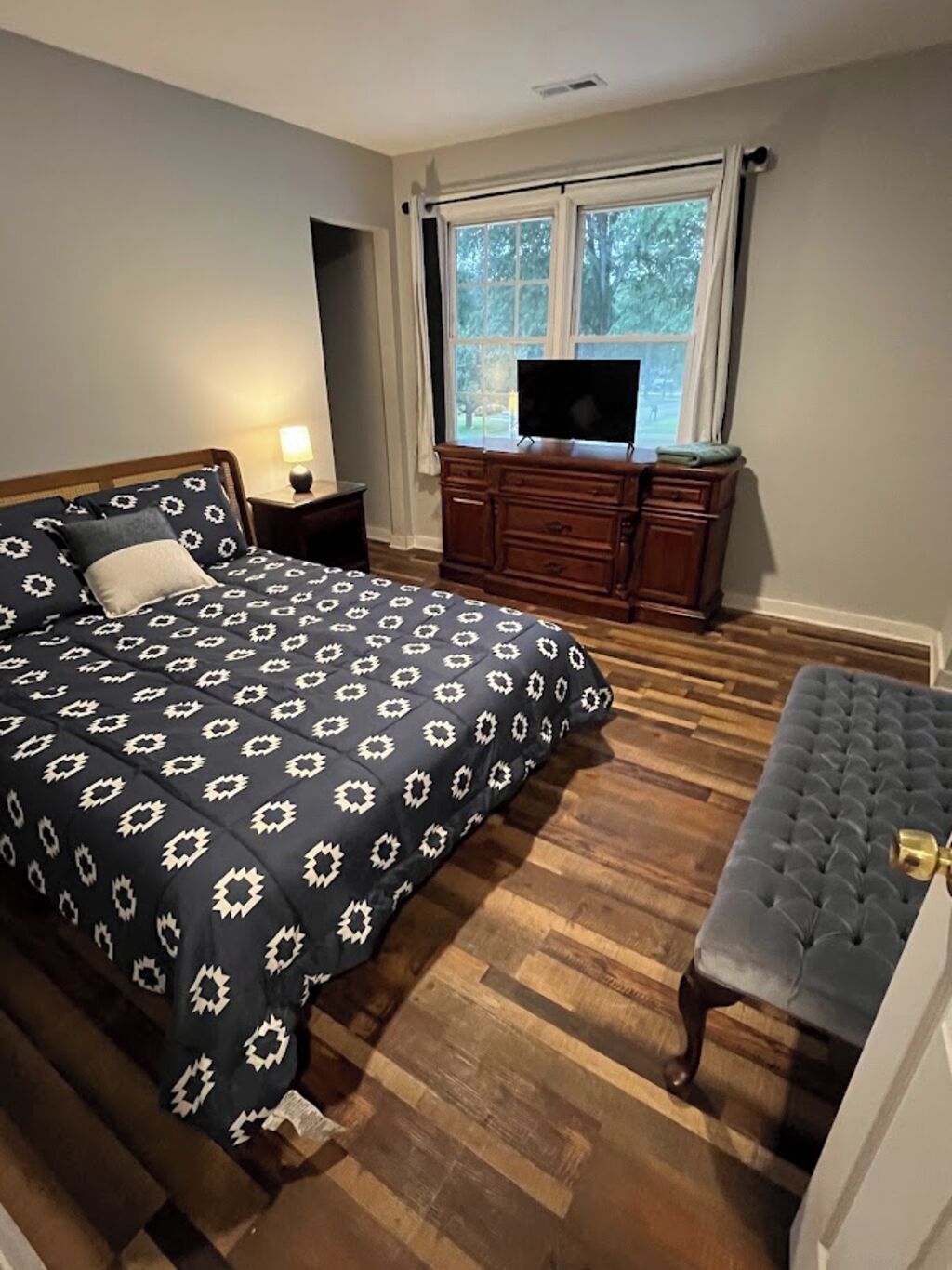 A bedroom with a bed, a nightstand, a dresser, a television, and a bench.