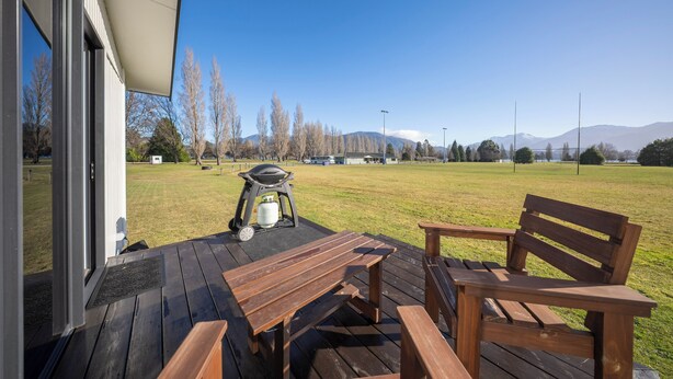 Eine Terrasse mit Holzmöbeln, einem Grill und Blick auf ein Wiesenfeld und Berge.
