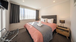 Ein Hotelzimmer mit einem Bett, einem Nachttisch mit Lampe, einem Fenster mit Vorhängen und einem Sessel.