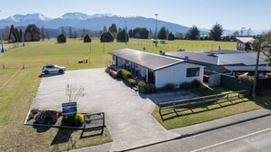 Ein Motel mit Parkplatz, ein kleines Gebäude mit überdachter Terrasse und Blick auf Berge im Hintergrund.