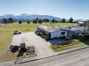 A motel with a parking lot, a small building with a covered patio, and a view of mountains in the background. - Dusky Rugby Unit - Te Anau Holiday Home (Te Anau)
