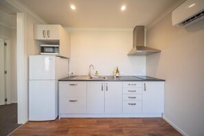 A modern kitchen with white cabinetry, a built-in microwave, a stainless steel sink, and a range hood. - Dusky Rugby Unit - Te Anau Holiday Home (Te Anau)