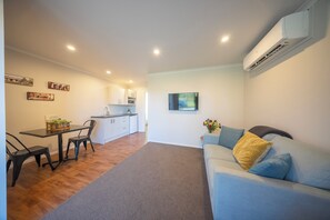A modern living room with a sofa, a dining area with a table and chairs, a kitchen with cabinets, and a mounted TV. - Dusky Mustering Unit - Te Anau Holiday Home (Te Anau)