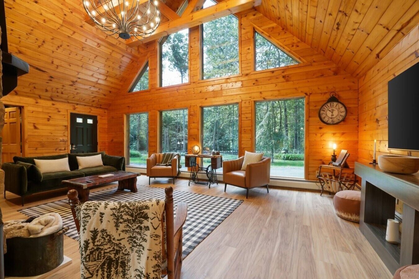 Ein Blockhaus-Interieur mit Kamin, großen Fenstern, einer Couch und einem Essbereich.