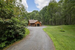 A rustic cabin with a paved driveway leading to it, surrounded by dense forest. - The Log Cab-Inn - Hot Tub - Game Room - PS5 - Poconos Gem - Rustic Luxury (Albrightsville)