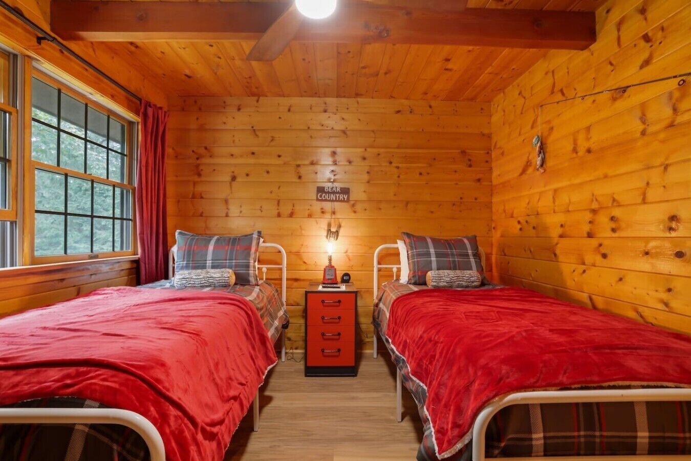 A cabin with two beds, a red blanket on each, a small table with a lamp, and a sign that reads 'BEAK COUNTRY'.