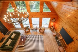 Interior acogedor de una cabaña con un ventanal grande, una lámpara de araña, un sofá y un televisor.