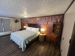 Quarto de hotel com cama, duas luminárias de cabeceira, mesa de cabeceira, cômoda de madeira e ventilador de teto.