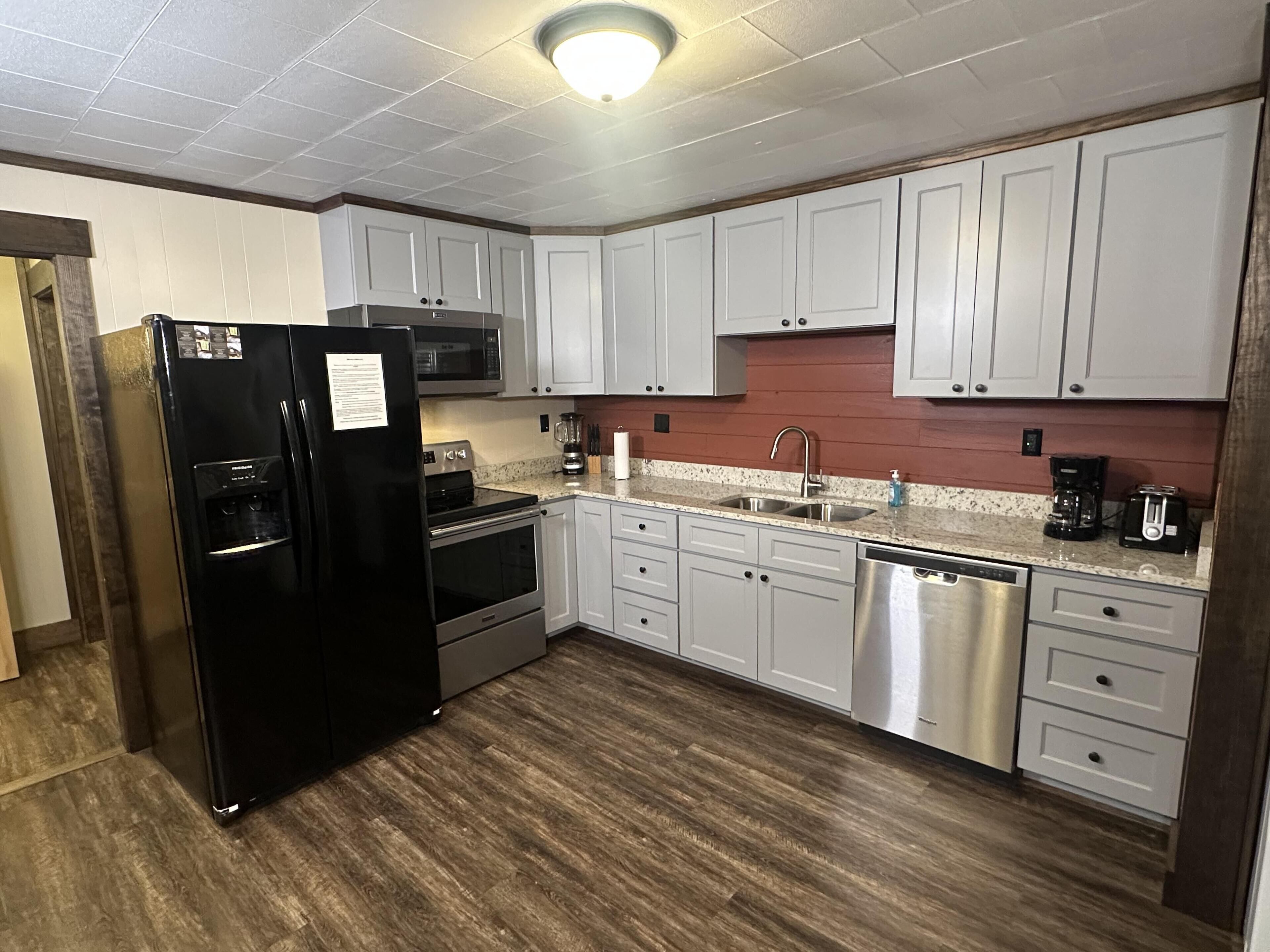 A modern kitchen with white cabinets, stainless steel appliances, and a wooden floor.