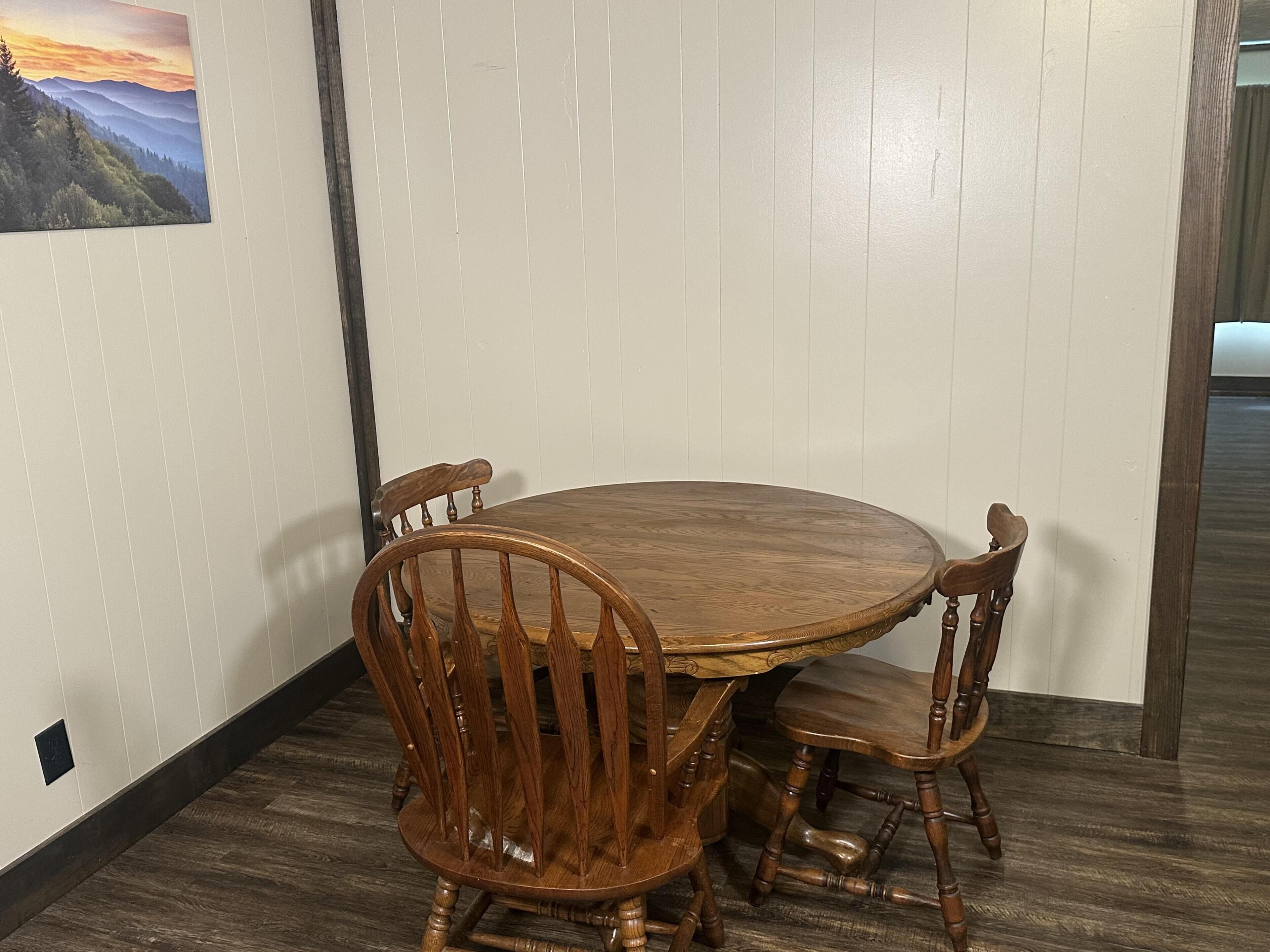 Een eetgedeelte met een ronde houten tafel en vier stoelen, een houten vloer en een witte muur met een afbeelding.