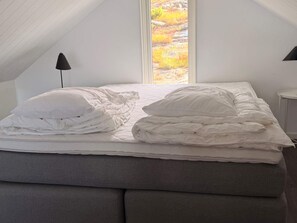 A bedroom with a sloped ceiling, a bed with white bedding, and a view of a rocky landscape through a window. - 5 Star Holiday Home in Uddevalla (Uddevalla)