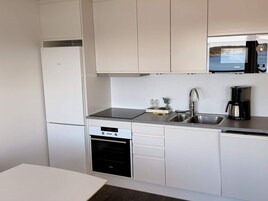 Una cocina moderna con armarios blancos, horno empotrado, microondas y cafetera.