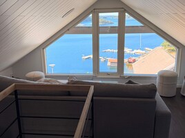 Una habitación con techo inclinado, un ventanal con vistas al mar y al puerto, y un sofá con cojines.