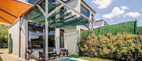 A modern house with a covered outdoor area, a swimming pool, and a well-maintained garden.