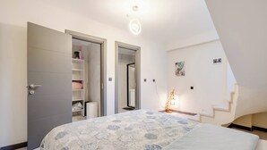 A bedroom with a bed, a wardrobe, a bedside table with a lamp, and a staircase.
