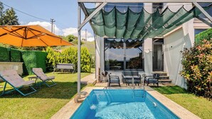 A swimming pool with lounge chairs, a covered patio, and a view of the house.