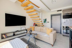 A modern living room with a sofa, a coffee table, a TV, and a staircase.