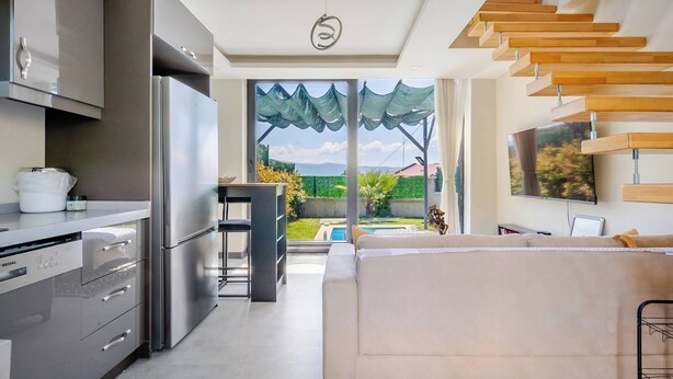 A modern kitchen with stainless steel appliances, a dining area with a table and chairs, a sofa, and a large window overlooking a garden.