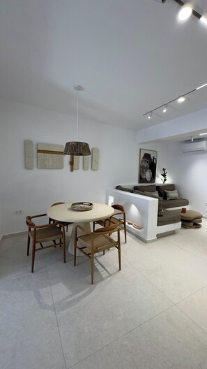 A modern living room with a dining area, featuring a round table, wooden chairs, a hanging lamp, and a sofa. - Borgo Stampalia – Villa Sabbia (Astypalea)