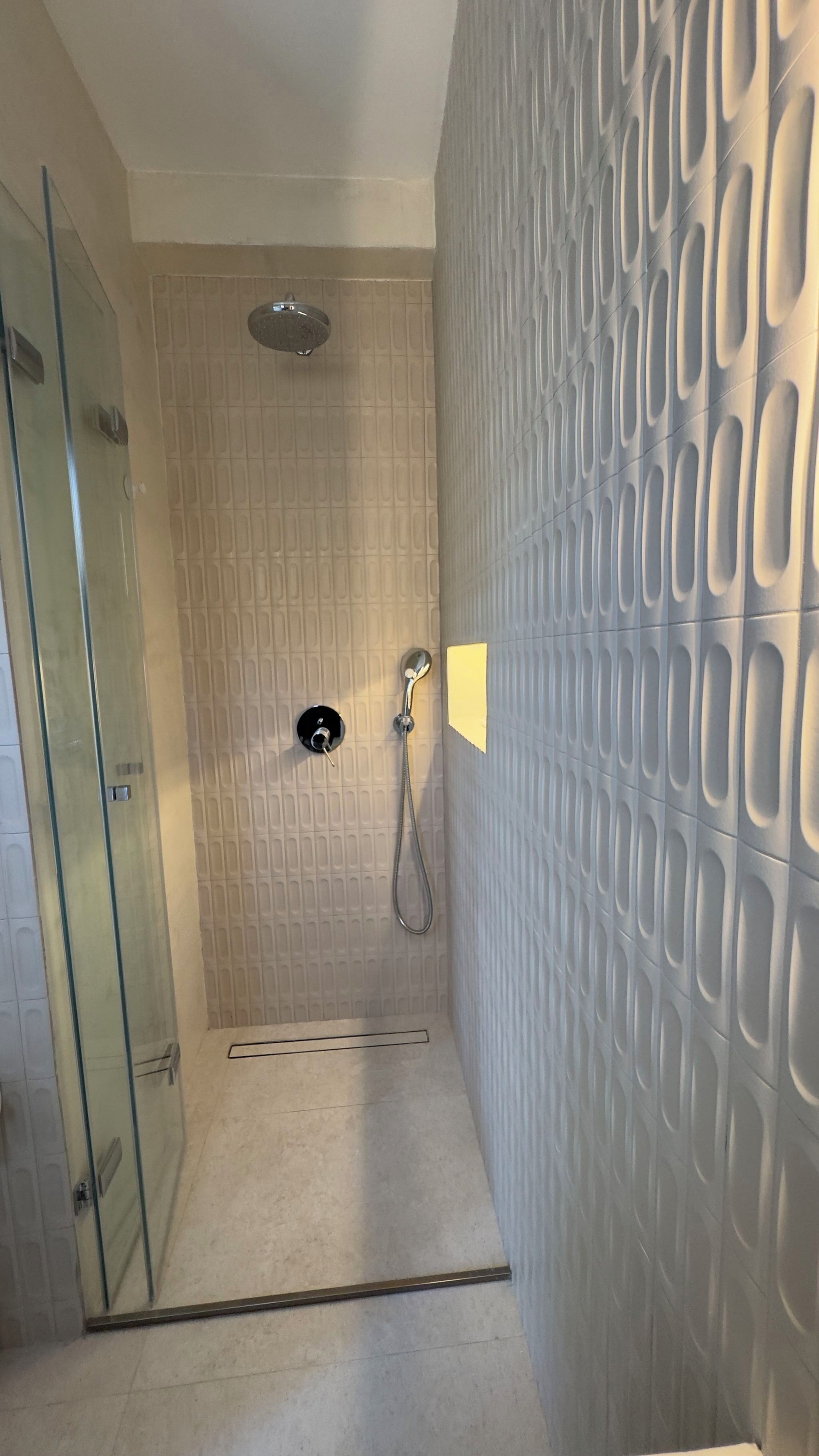Un espace douche doté d’une porte en verre, d’un pommeau de douche et d’un mur au motif texturé.