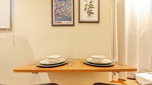 Una mesa de comedor con platos, cubiertos y vasos, frente a una pared lisa con dos obras de arte enmarcadas.