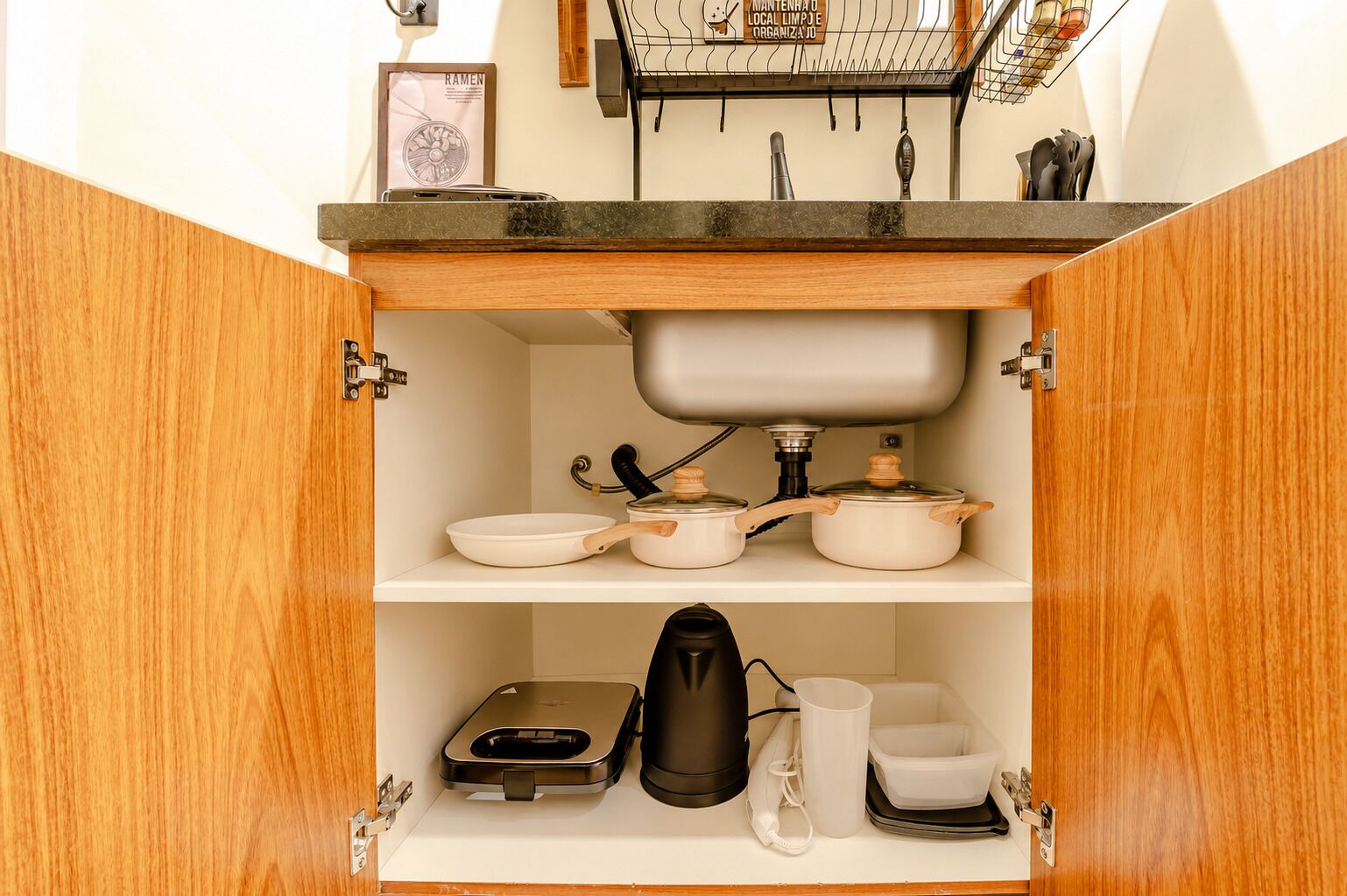 Una cocina con armarios de madera, un lavamanos y diversos utensilios de cocina, incluyendo ollas, sartenes y un hervidor.