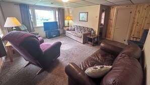 A living room with a leather sofa, a purple armchair, a television, and a wooden door. - 3-bedroom Waterview cabin with AC in charming Birchwood | Waterview Cabin with Private Boat Slip (Birchwood)