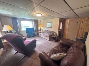A living room with a leather sofa, a purple armchair, a television, and a wooden door. - 3-bedroom Waterview cabin with AC in charming Birchwood | Waterview Cabin with Private Boat Slip (Birchwood)