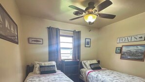 A room with two single beds, a ceiling fan, a window with curtains, and a wall sign indicating 'BOATS'. - 3-bedroom Waterview cabin with AC in charming Birchwood | Waterview Cabin with Private Boat Slip (Birchwood)