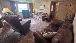 A living room with a sofa, armchair, TV, and a lamp. - 3-bedroom Waterview cabin with AC in charming Birchwood (Birchwood)