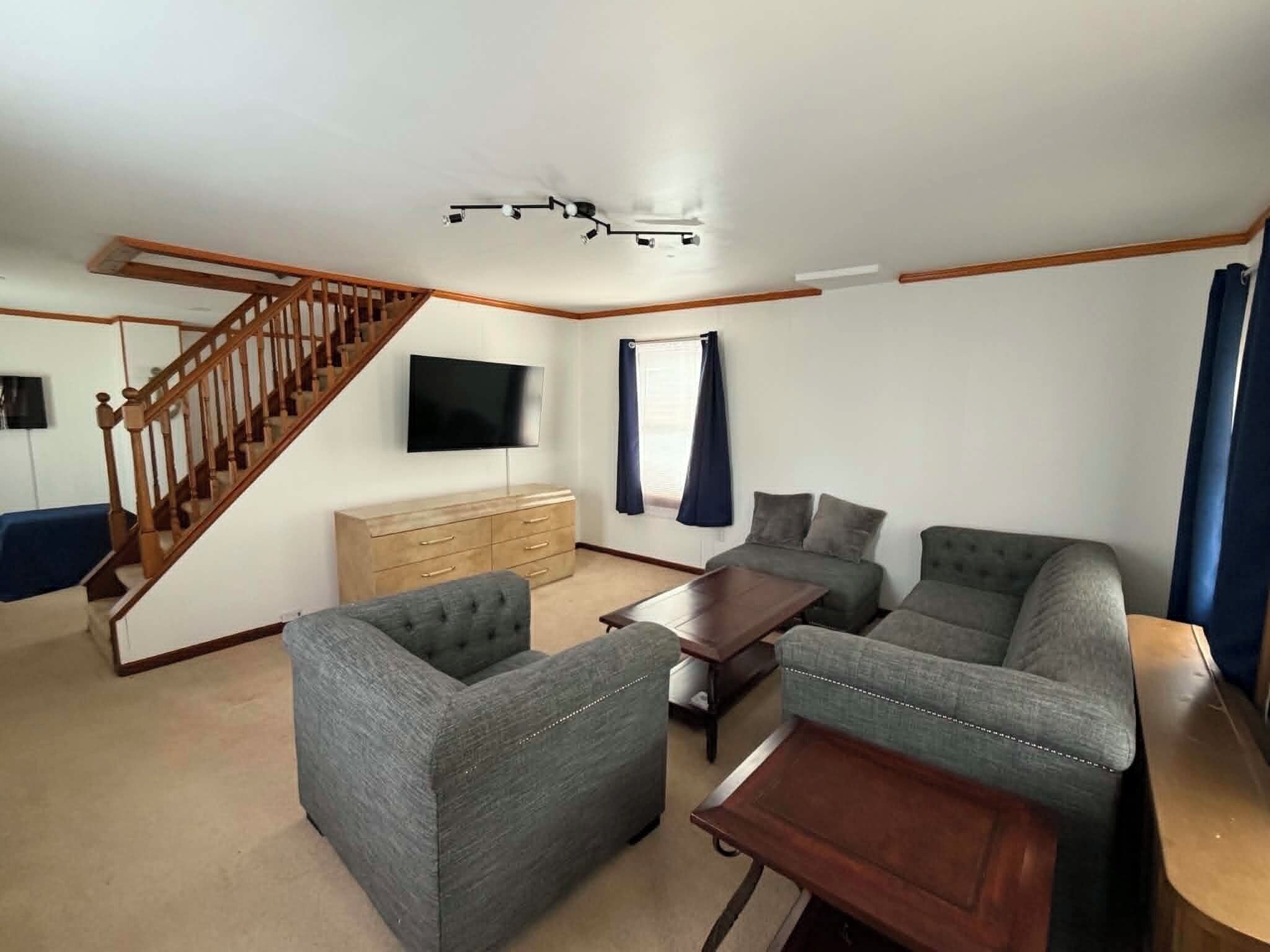Ein Wohnzimmer mit Treppe, Flachbildfernseher, Holzkommode und zwei grauen Sofas.