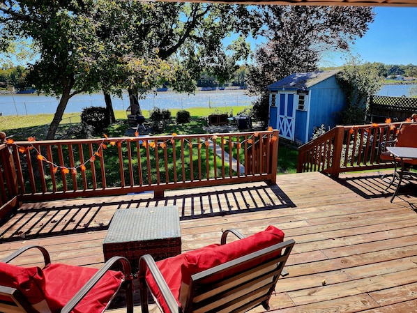 Une terrasse en bois avec des meubles d’extérieur, un petit abri de jardin et une vue sur une étendue d’eau.