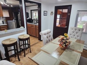 Une cuisine moderne avec des meubles en bois, un réfrigérateur en acier inoxydable et un coin repas comprenant une table en bois et deux tabourets de bar.