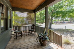 Eine hölzerne Veranda mit einer Bank und Stühlen, einem Blumentopf und Blick auf eine Straße und einen Spielplatz.