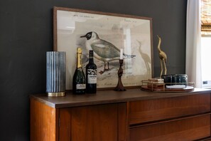 Eine gerahmte Vogelillustration, eine Weinflasche, eine Kerze und eine dekorative Vogelstatue auf einem Holzschrank.