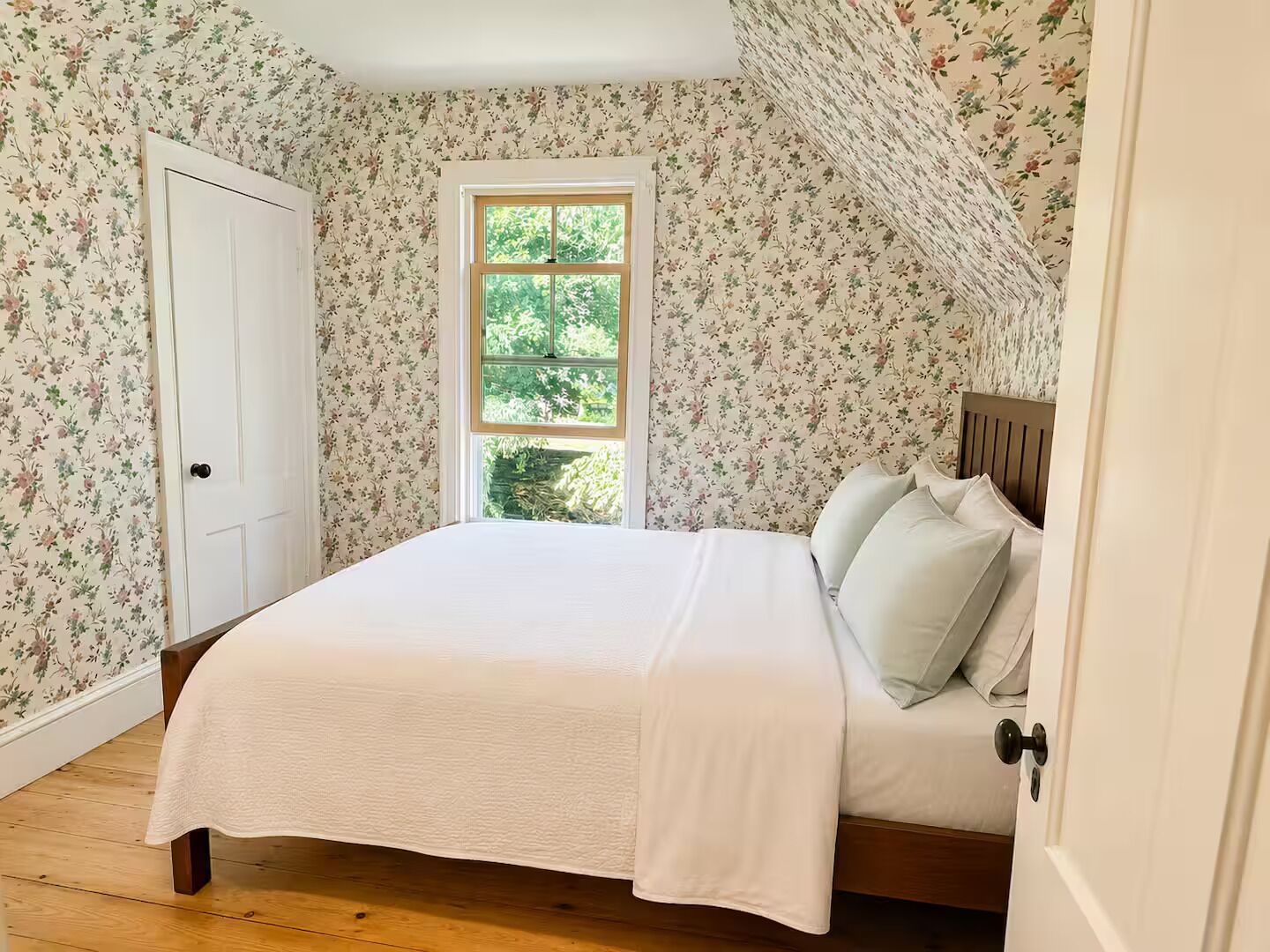 Un dormitorio con una cama individual, una ventana y papel tapiz con motivos florales.