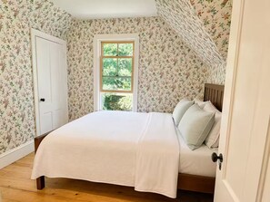 A bedroom with a single bed, a window, and floral wallpaper. - The Owl's Roost Manor in Owl's Head, ME (Owls Head)